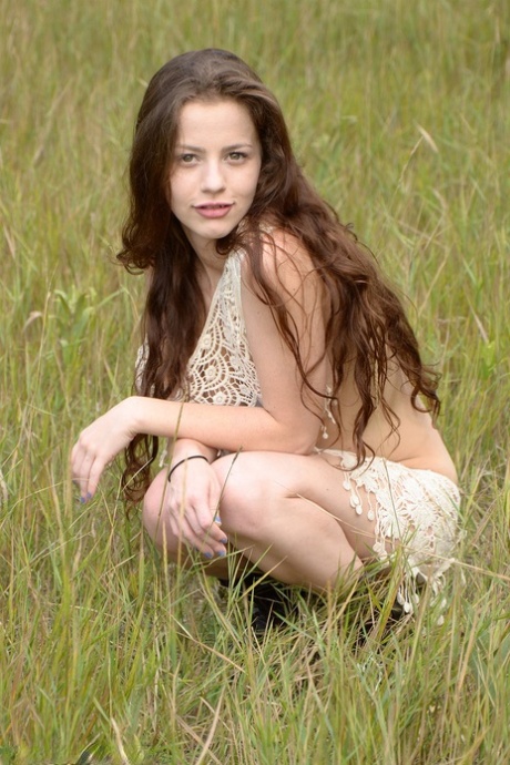 Young girl with long wavy hair Iva Nora gets naked in a field
